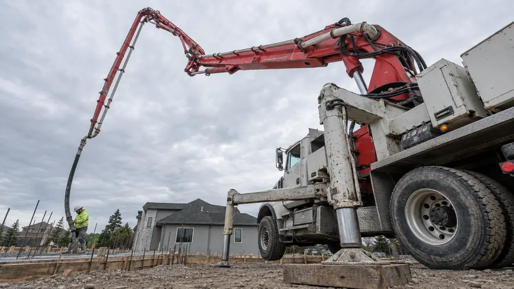 A concrete pump truck with its boom extended over a residential foundation